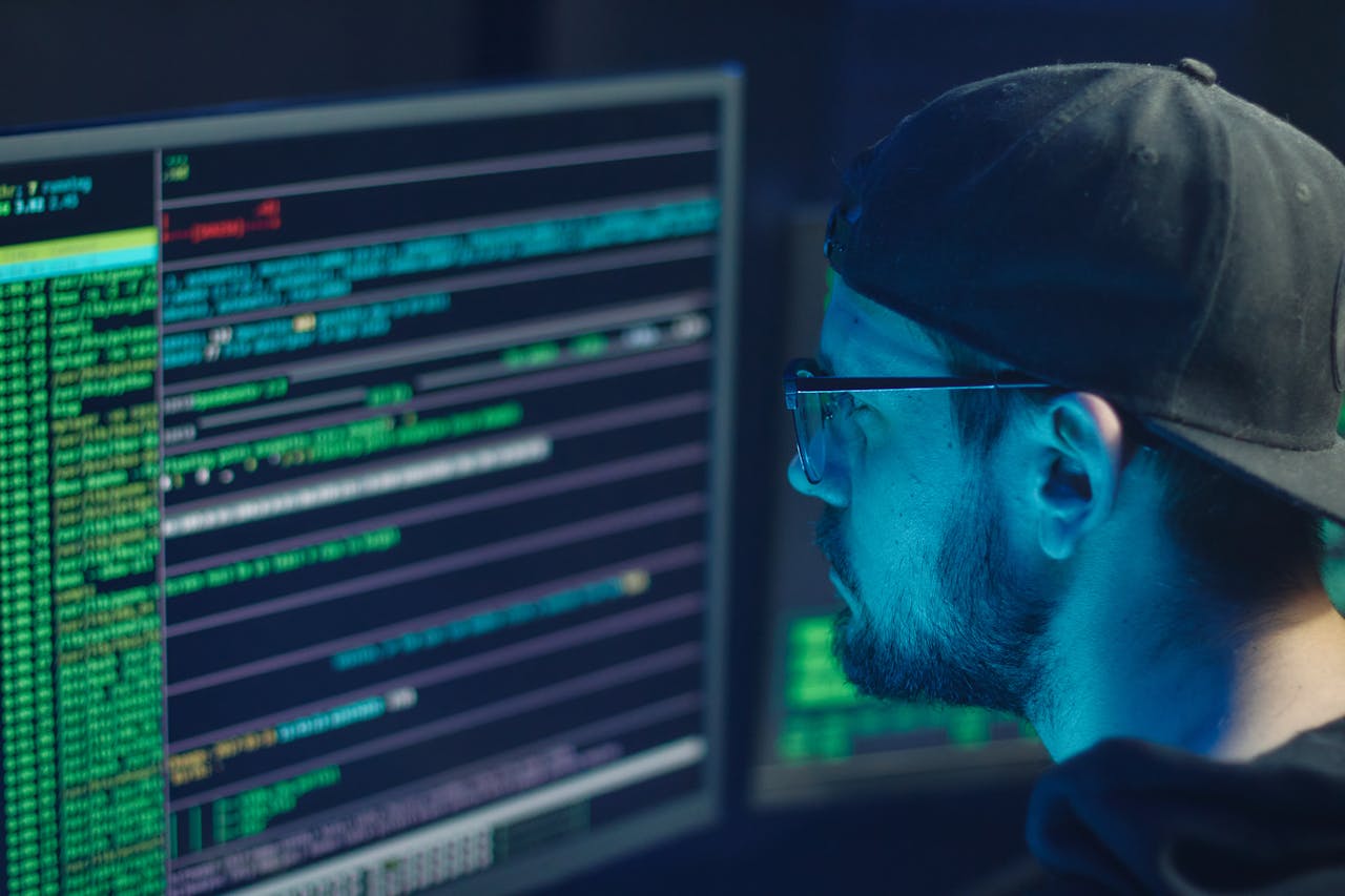 heros-img A cybersecurity expert inspecting lines of code on multiple monitors in a dimly lit office.